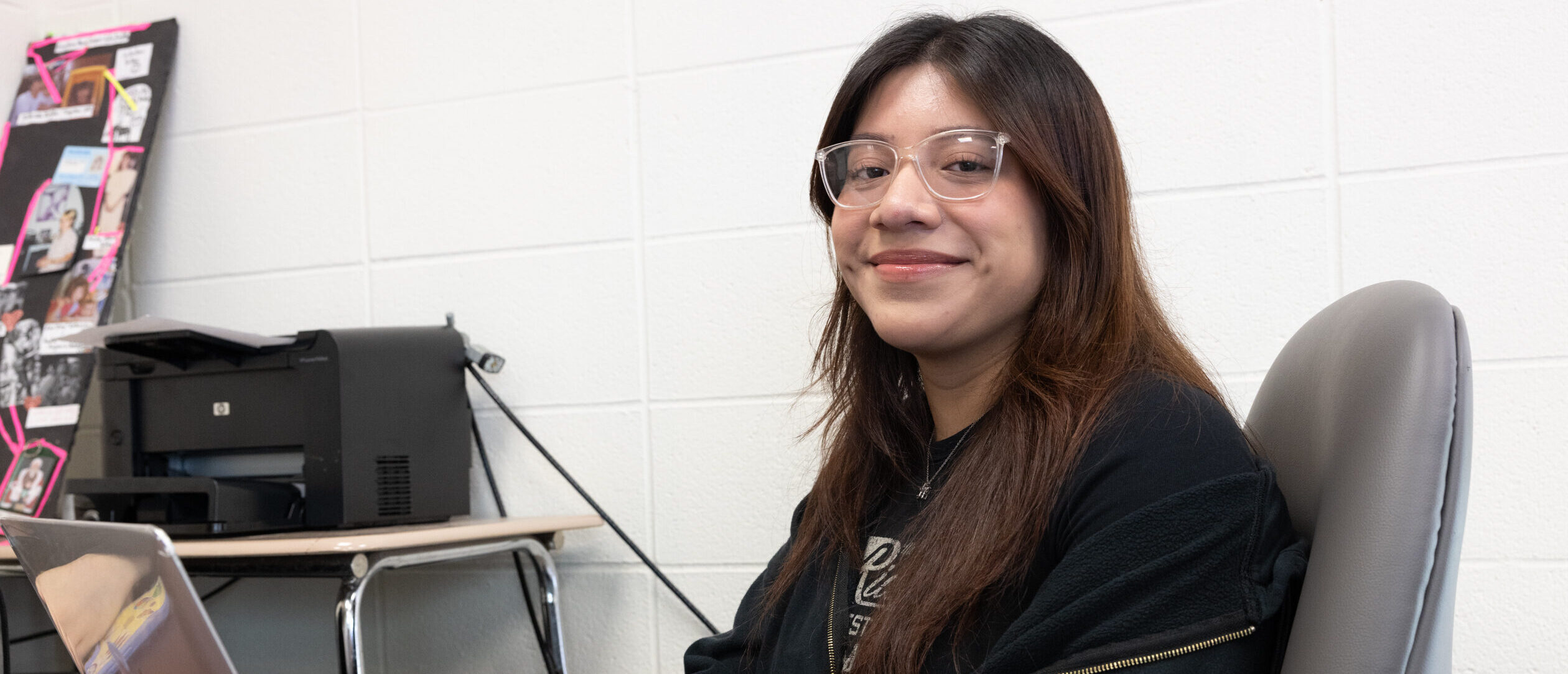 student smiling at camera working on laptop